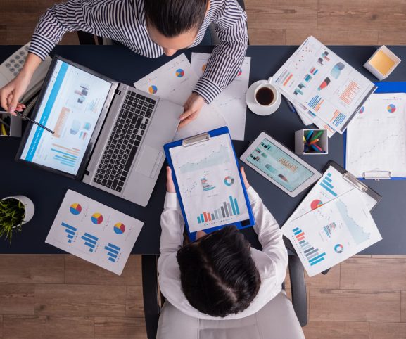 Top view of manager and employee doing teamwork Top viewTop view of manager and employee doing teamwork in business office , looking at charts on laptop display. Finance paperwork with charts at workplace. Discusing financial plan.